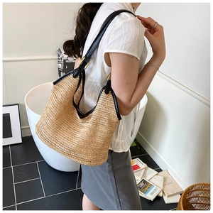 Detail showing the black leather trim and gold metal buckle on a straw woven tote bag