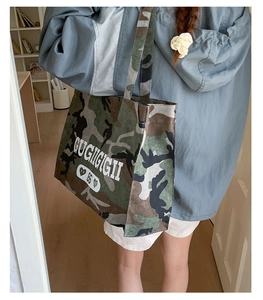 Side view of large camouflage canvas tote bag with GUGIIGIGII text print on woman's shoulder