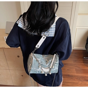 Detail of green striped tote bag with silver chain and pearl charm on white strap