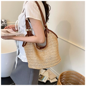 Close-up of woven straw tote bag with brown leather trim and golden metal buckles