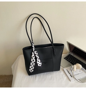 Close-up of black litchi grain leather tote bag with stylish polka dot scarf on handle