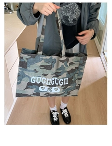 Detail of large camo canvas tote bag with white text GUGHIGUGII and number 86 logo