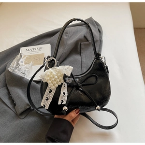 Détail du sac croissant en cuir verni noir avec nœud et breloque en dentelle perlée