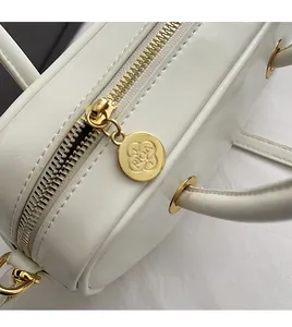 Detail of white leather handbag featuring gold zipper with embossed circular puller