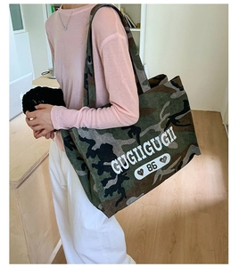Detail view of camouflage tote bag with white letter print worn over the shoulder