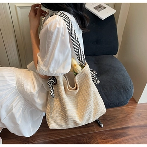 Detail of a straw tote bag with woven bow and wide striped strap on a model