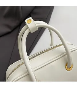 Detailed close-up of white leather handbag handles with durable gold metal hardware