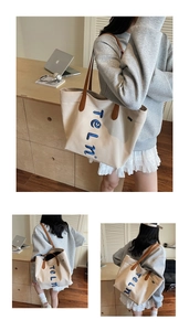 Detail of canvas tote bag featuring blue letter embroidery and brown leather handles