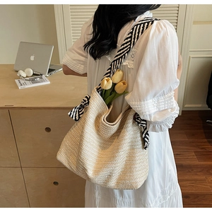Detail of woven straw tote bag with black and white striped strap in a cozy home setting