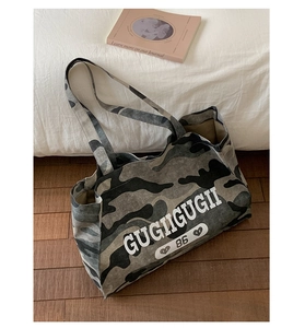 Top view of camouflage tote bag with letter print on white bedding and wood floor