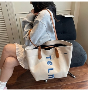 Detail view of large canvas tote bag featuring blue letter embroidery and leather handles