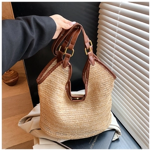 Close-up of woven straw handbag with brown leather handles and gold metal buckles