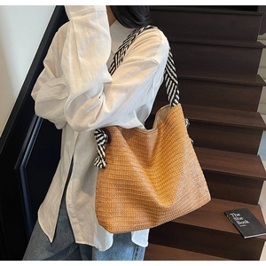 Detail of hand-woven straw tote bag with black and white striped rope shoulder straps