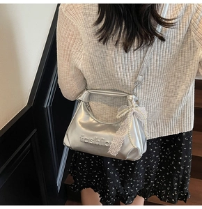 Silver faux leather bag with pearl bow charm and embossed detail shown on a model
