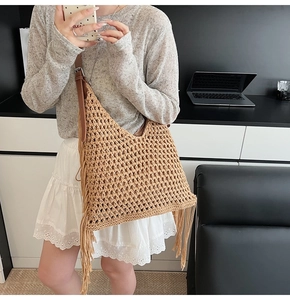 Detail shot of khaki woven straw tote bag featuring long fringes and brown leather strap