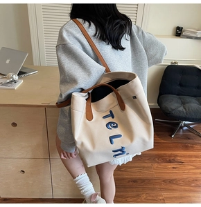 Detail showing high-capacity canvas tote bag with embroidered letters and brown leather straps
