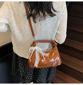 Detail view of brown glossy oil-wax leather crossbody bag with lace pearl charm
