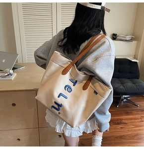 Detail of canvas tote bag with blue embroidered letters and brown leather strap