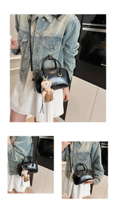 Detail of black matte leather handbag with gold rings and cute bear plush charm