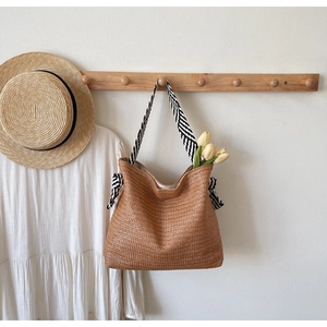 Detail of woven straw tote bag with striped shoulder strap and decorative fabric knot