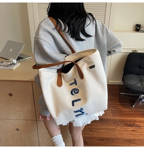 Detail of white canvas tote with brown leather straps and blue letter embroidery