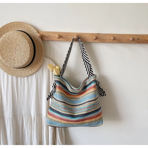 Detail of colorful woven straw shoulder bag with striped bow and black and white handles