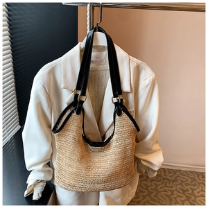 Close-up of woven straw tote bag with black leather straps and golden metal hardware