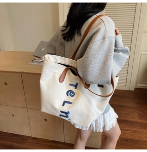 Detail of white canvas tote bag featuring blue embroidery and brown leather straps