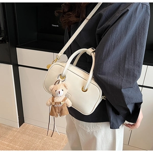 Detailed side view of white faux leather crossbody bag with teddy bear pendant and gold rings