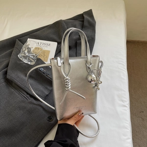 Dettaglio della borsa metallizzata argento con decoro a nodo spesso e ciondolo a sfera