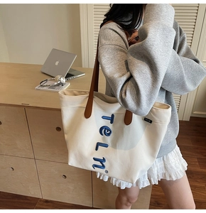 Detail of canvas tote bag showing blue letter embroidery and dark brown leather straps