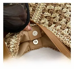 Close-up of the silver magnetic buckle and brown leather handle on a woven straw tote bag