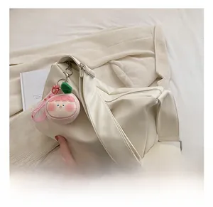 Detail view of cream white PU tote bag with a pink smile charm and wide shoulder strap