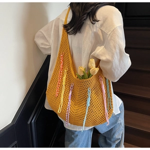 Detail of yellow hollow knit tote bag with colorful rainbow tassels on wooden stairs