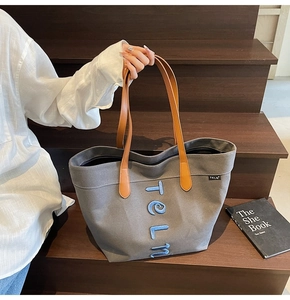 Close-up of deep grey canvas tote bag featuring blue letter embroidery and leather handles