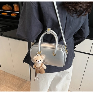 Silver metallic crossbody bag with round handles and a cute teddy bear plush charm