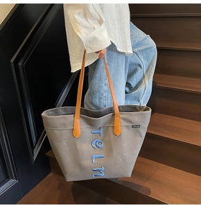Detail of grey canvas tote bag featuring orange leather handles and blue teln embroidery