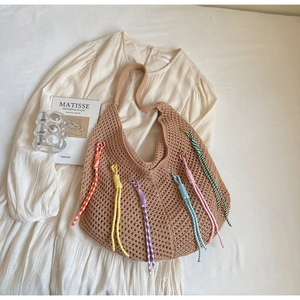 Close-up of bohemian woven tote bag with colorful tassels on white summer dress