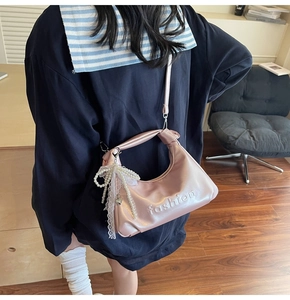 Detail of pink faux leather bag featuring embossed fashion text and pearl bow charm