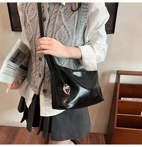 Close-up of black patent leather shoulder bag with a silver heart-shaped metal pendant