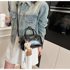 Detail of black glossy handbag featuring gold ring buckle and cute teddy bear charm