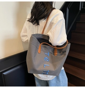 Detail of grey canvas tote bag with blue embroidery and leather handles on model