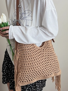 Handmade woven hollow straw tote bag with boho tassels and leather strap worn by a model