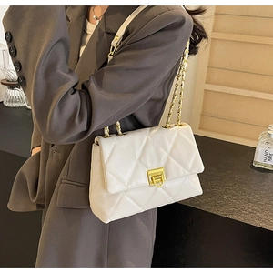 Détail d'un sac blanc matelassé avec chaîne dorée porté sur un blazer marron