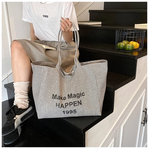 Close-up of black and white striped tote bag with Make Magic Happen text in street setting