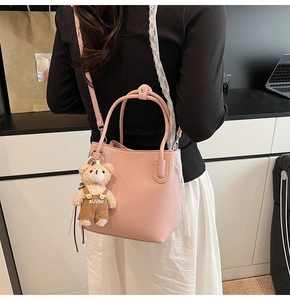 Pink bucket bag detail with plush bear charm and textured litchi grain leather finish