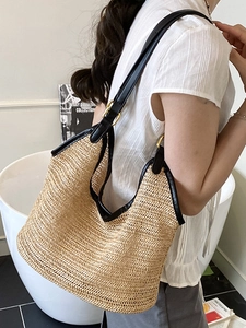 Minimalist woven straw beach bag with black leather shoulder straps and golden hardware