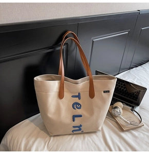 Detail view of canvas tote bag with embroidered letters, laptop, and lifestyle accessories