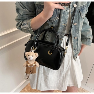 Detail of black glossy handbag with gold metal eyelets and a cute brown plush bear charm
