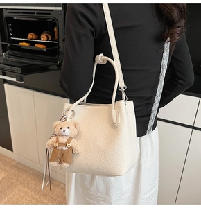 Detail of a creamy white litchi grain bucket bag with a cute plush bear charm on its side